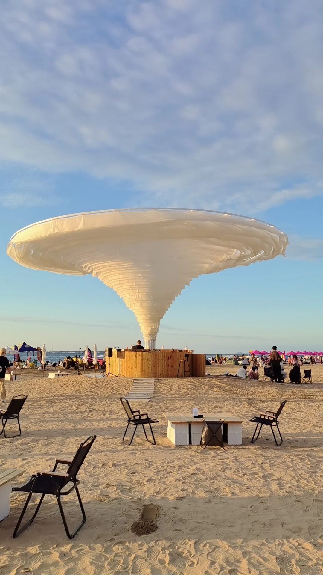 massive white tornado-shaped fabric canopy against sunset sky on beach